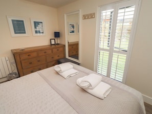 A bedroom with a bed, a dresser, a mirror, and a window with blinds. - Summerset Lodge (Bamburgh)