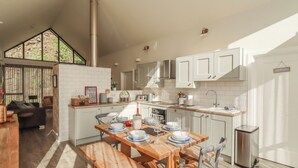 A modern kitchen with white cabinets, a dining table set for four, and a large window overlooking a natural landscape.