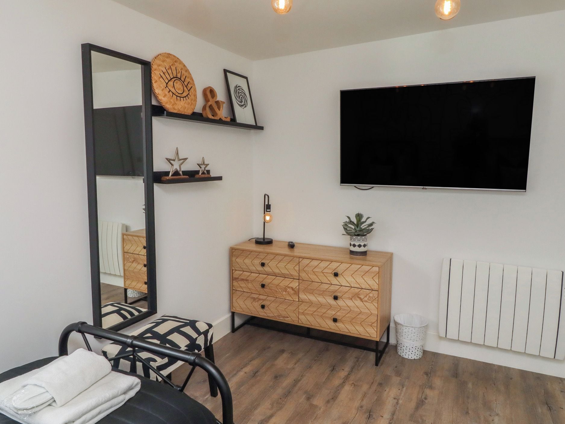 Een moderne kamer met een grote spiegel, een houten dressoir, een flatscreen televisie en een radiator.
