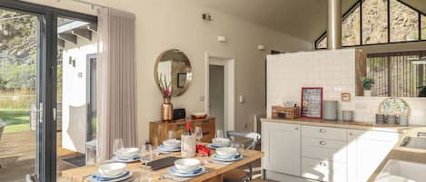 A modern kitchen with white cabinets, a wooden dining table set for six, and a large window with a view of the outdoors.