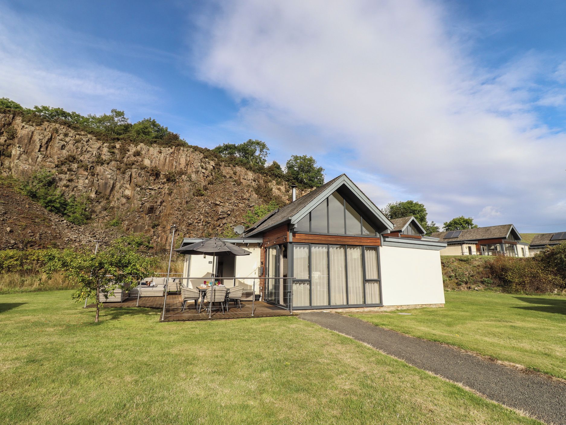 A modern house with a large glass door, a patio with outdoor furniture, and a view of a rocky hillside.