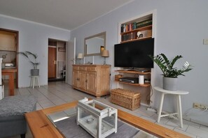 A living room with a television, bookshelves, a wooden cabinet, a plant, and a dining area. - Stylish and authentic vacation rental in Friedrichskoog – Perfectly located (Friedrichskoog)