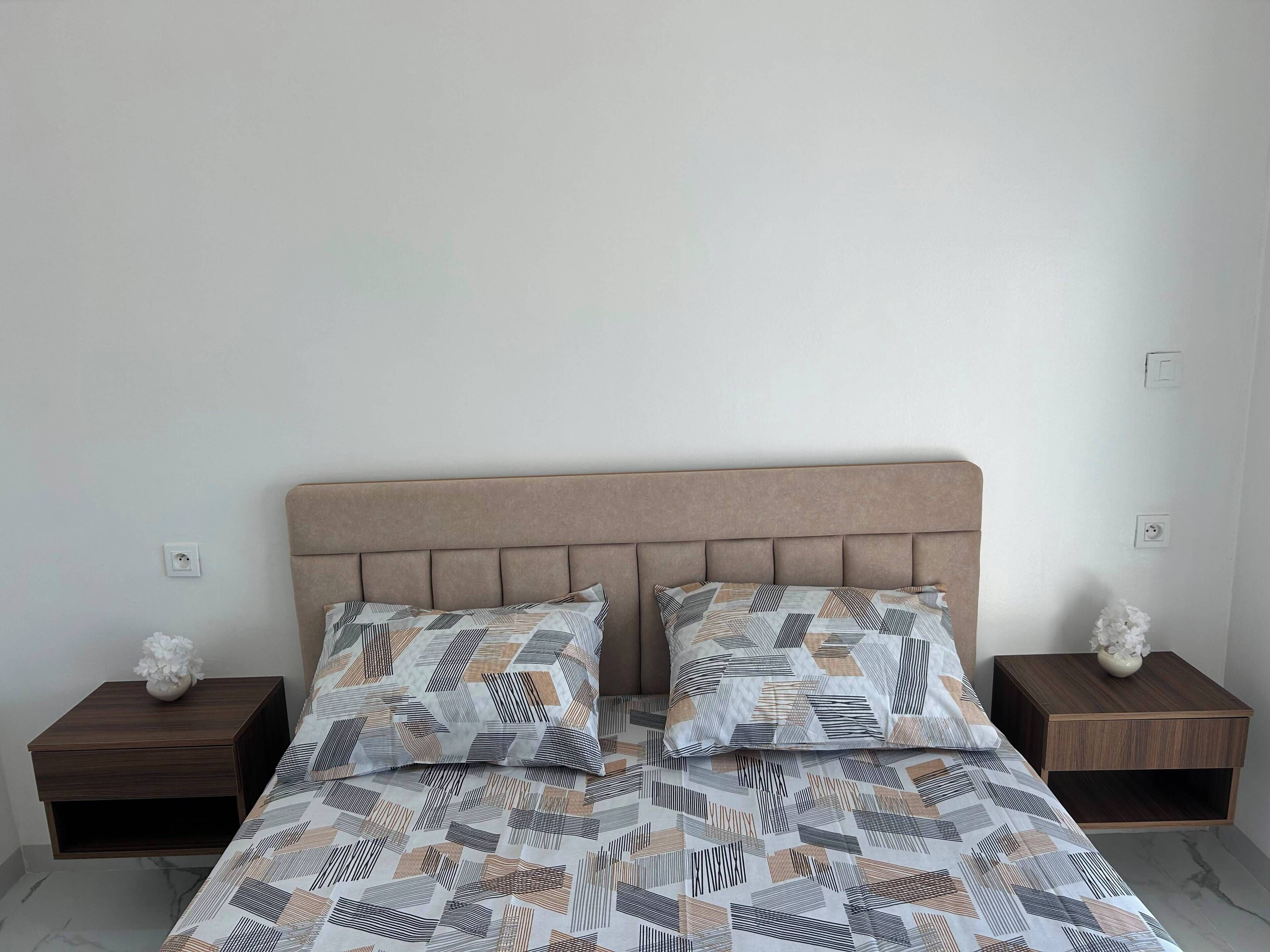 A bed with a patterned bedspread and two pillows, flanked by wooden nightstands with decorative vases.