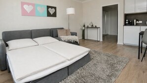 A modern bedroom with a grey sofa bed, a bedside table with a lamp, and a wall with heart-shaped artwork. - The "Kaiserhof 1" vacation rental. (Norderney)