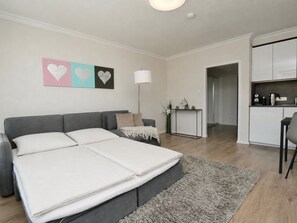 Ein modernes Schlafzimmer mit einem grauen Schlafsofa, einem Nachttisch mit Lampe sowie einer Wand mit herzförmiger Dekoration.