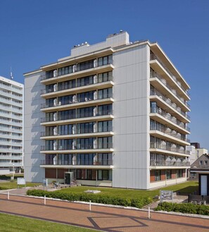Ein mehrstöckiges Hotel mit Balkonen, einem Ziegelweg und blauem Himmel.