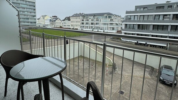 A balcony with two wicker chairs and a glass table, overlooking a parking area and buildings. - The "Kaiserhof 1" vacation rental. (Norderney)