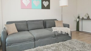 A grey sofa with two pillows, a white throw blanket, and a fluffy grey rug. - The "Kaiserhof 1" vacation rental. (Norderney)
