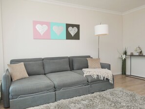 Ein graues Sofa mit zwei Kissen, einer weißen Tagesdecke und einem flauschigen grauen Teppich.
