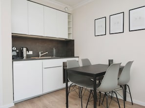 Een moderne keuken met witte kasten, een donker aanrecht en een eettafel met stoelen. Er hangen ingelijste foto's aan de muur.