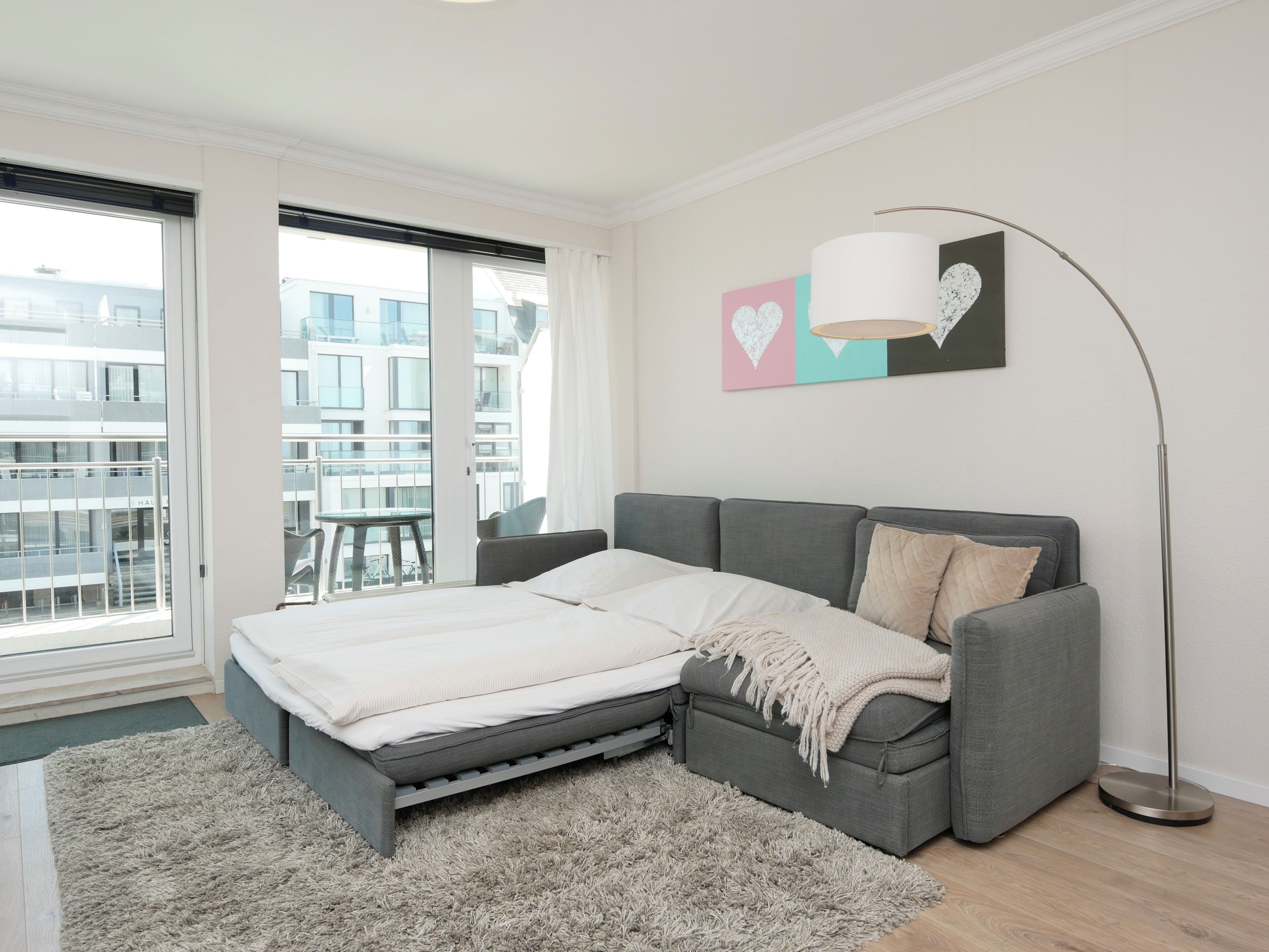 A modern bedroom with a bed, grey sofa, and a large window.