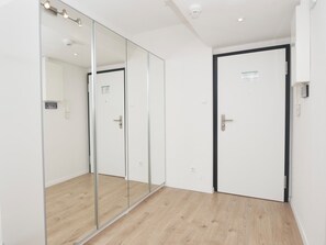 Ein Flur mit einem raumhohen Spiegelkleiderschrank, einer Tür mit schwarzem Rahmen und einem Lichtschalter an der Wand.