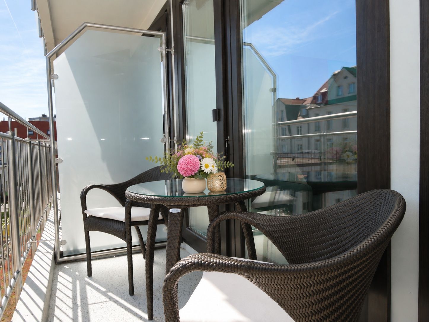 A balcony with a glass table, wicker chairs, and a vase with flowers.