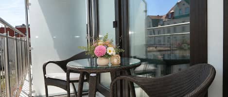 A balcony with a glass table, wicker chairs, and a vase with flowers.