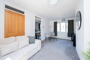 Un salon avec un canapé blanc, une table à manger avec des chaises, une porte en bois et un grand miroir au mur.