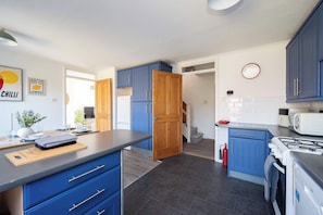 A kitchen with blue cabinets, a wooden door, a white refrigerator, a microwave, and a stove. - Stylish 3-Bed Home - 10 Min Gatwick - WiFi & Parking (West Sussex)