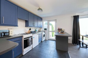 Une cuisine moderne avec des meubles bleus, une cuisinière à gaz, un lave-linge et un coin repas offrant une vue agréable.