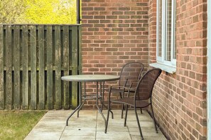 A patio with a brick wall, a wooden fence, and a table with chairs. - Stylish 3-Bed Home - 10 Min Gatwick - WiFi & Parking (West Sussex)