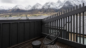 En balkon med udsigt til sneklædte bjerge, en stol og et lille bord.