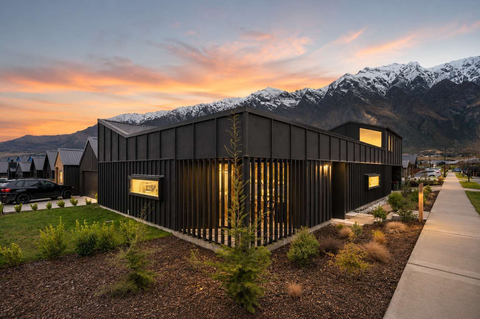 A modern building with a dark exterior, large windows, and a view of snow-capped mountains.