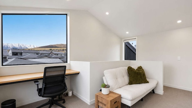 Et moderne kontorrum med skrivebord, stol og en hvid sofa med et lille bord og en plante.