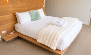 A bed with a wooden headboard, white bedding, a fluffy pillow, and a white blanket. - Simply Remarkables View in Hanleys |3 bed home (Jack's Point)