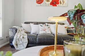 Ein modernes Wohnzimmer mit einem Ledersofa, einer weißen Decke und einem floralen Kissen.