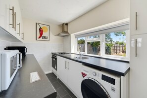 A compact kitchen with a microwave, dishwasher, and a window overlooking a backyard. - Cozy 1bed house with free parking (Buckinghamshire)