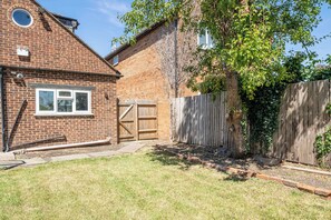 Une maison en briques avec un portail en bois, une cour clôturée et un arbre.