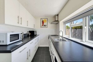 A modern kitchen with white cabinets, a black countertop, a microwave, a kettle, and a sink. - Cozy 1bed house with free parking (Buckinghamshire)