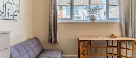 A room with a grey sofa, a wooden table, a window with curtains, and a wall with a geometric artwork.