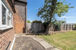 A residential backyard with a brick house, a wooden fence, and a grassy lawn. - Cozy 1bed house with free parking (Buckinghamshire)