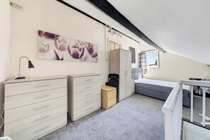 A bedroom with a bed, two dressers, a small cabinet, a desk with a lamp, a window with curtains, and a ceiling fan. - 5 Bed family house with free parking (Buckinghamshire)