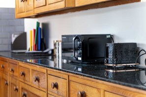 A kitchen with wooden cabinets, a black microwave, and a textured coffee mug on the countertop. - 5 Bed family house with free parking (Buckinghamshire)