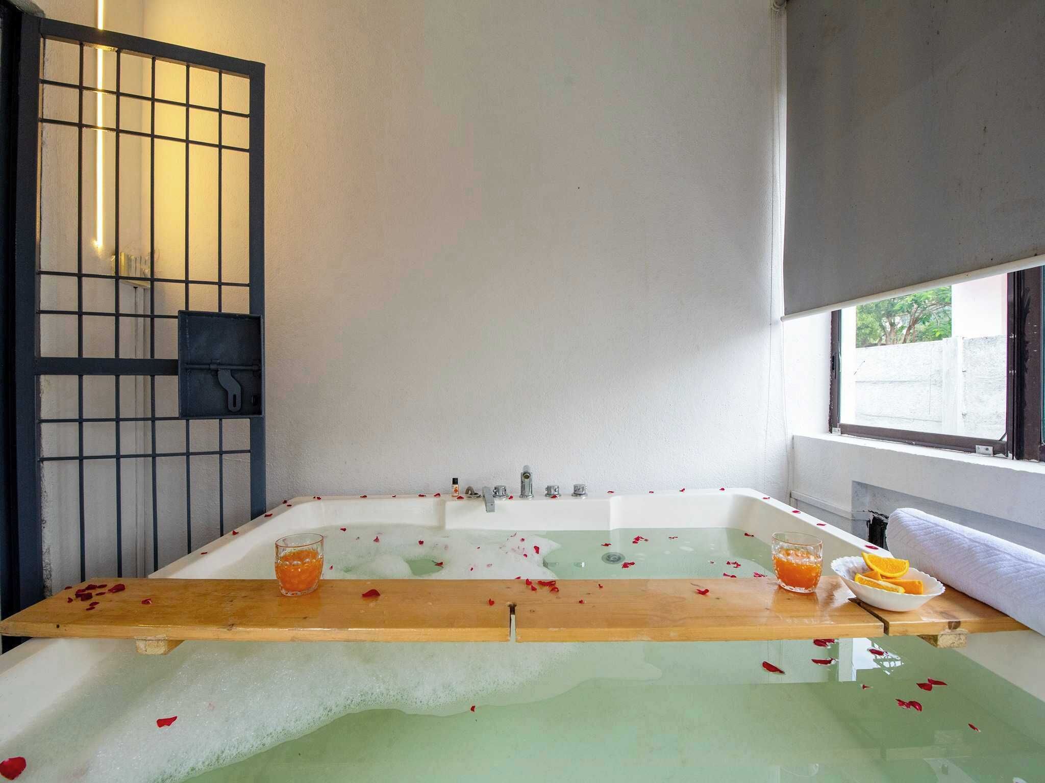 Une salle de bain avec une baignoire, un banc en bois et des pétales de rose sur le sol.
