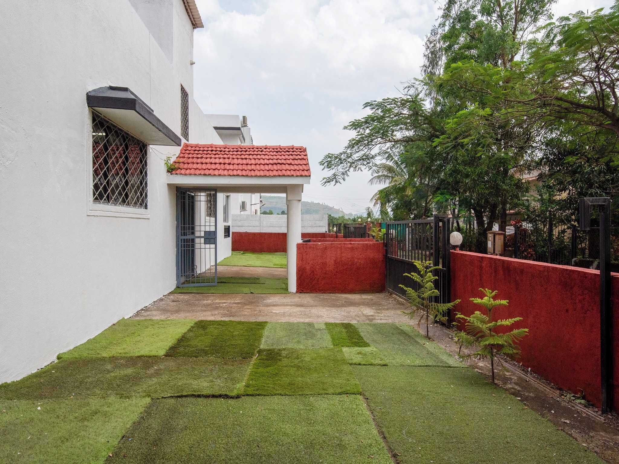 A residential property with a red-tiled roof, a white exterior wall, and a small garden area with artificial grass and a red wall.