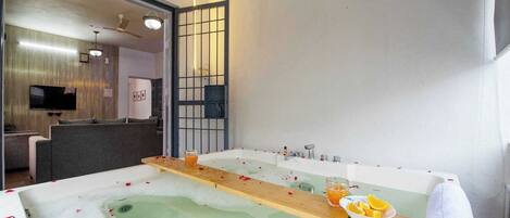 A spa room with a large bathtub, a wooden tray with fruits and a glass, and a towel rolled up.