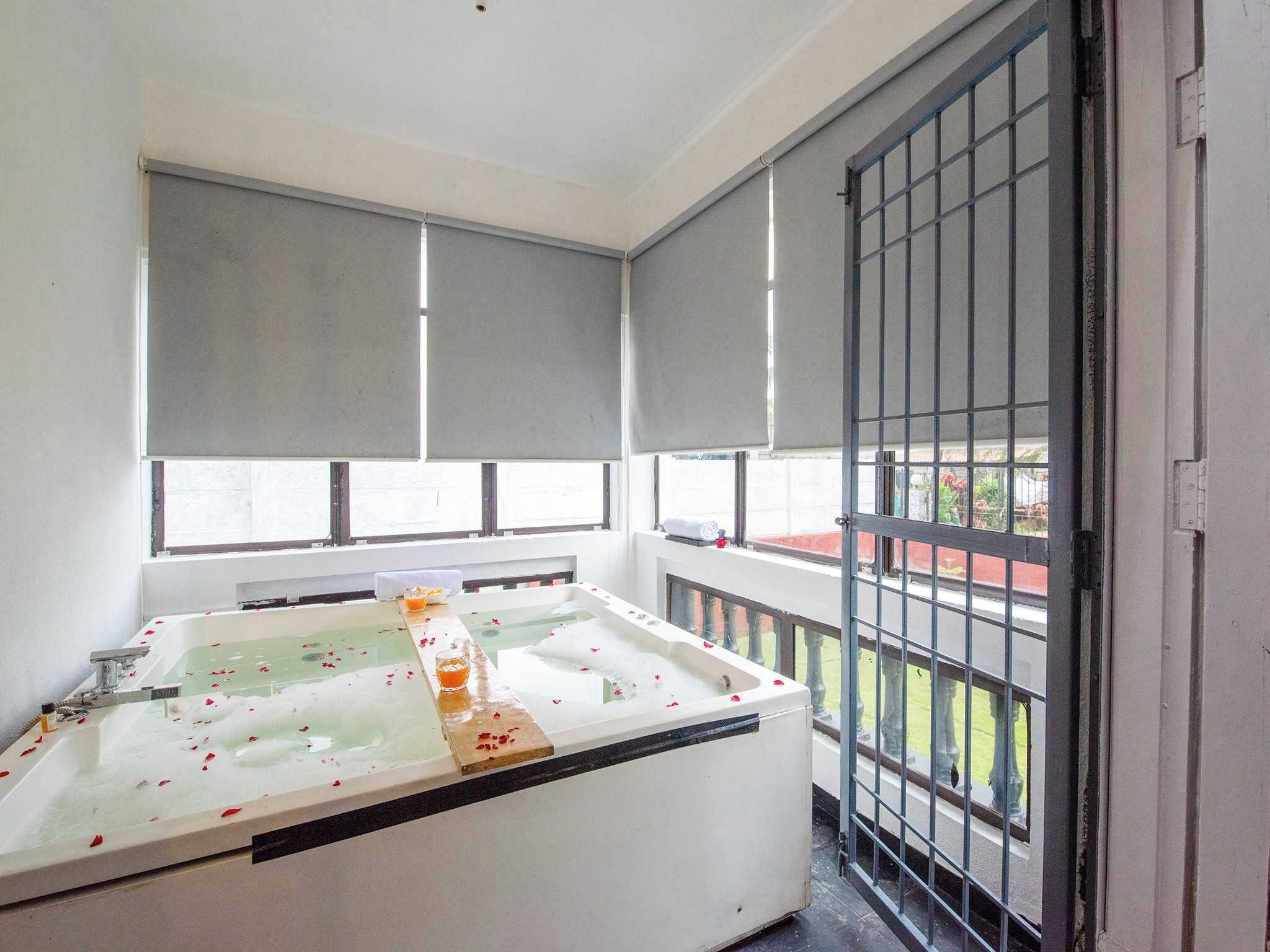 Een balkon met een badkuip, een raam met uitzicht op een rood gebouw en een metalen hek.