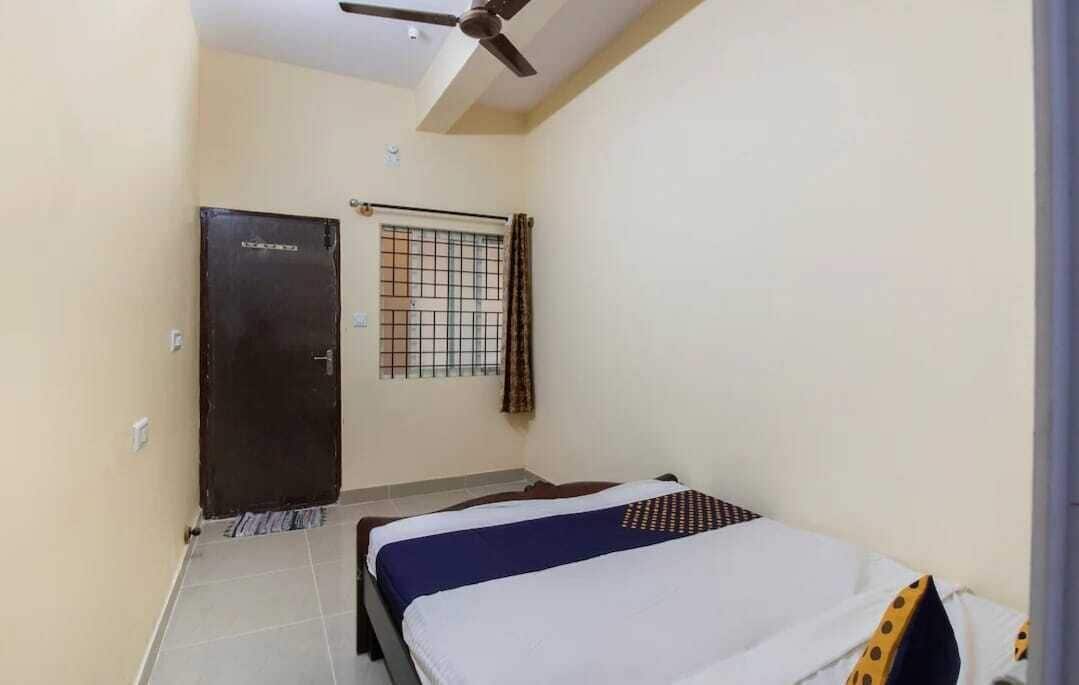 A room with a bed, a ceiling fan, a door, and a window with a metal grid.