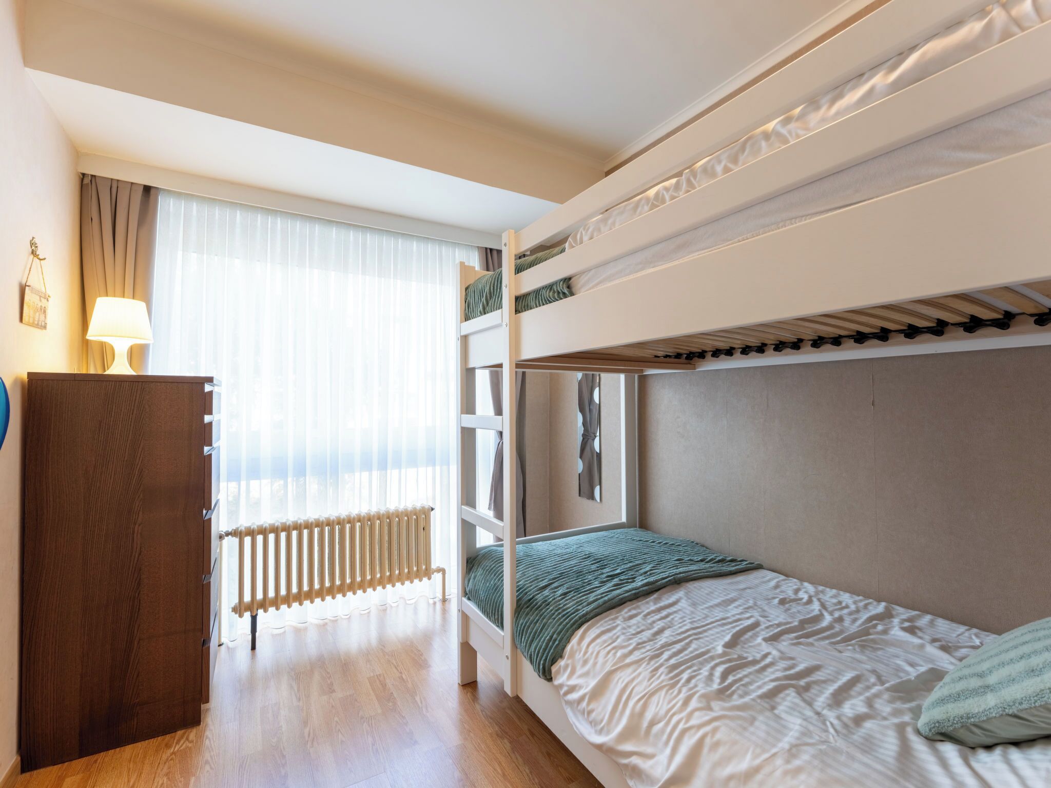 Ein Schlafraum mit Etagenbetten, einem Holzschrank, einem Heizkörper und einem Fenster mit Vorhängen.