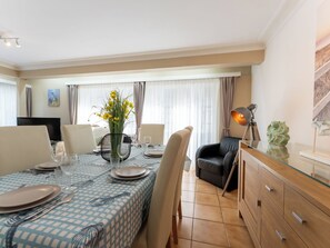 A dining area with a checkered tablecloth, a vase with flowers, and a television in the background. - Centrally located Sea You Again by Interhome (Blankenberge)