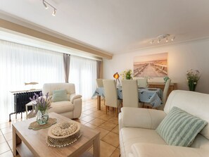 Ein Wohnzimmer mit einer Couch, Sesseln, einem Couchtisch und einem Essbereich mit Tisch und Stühlen.