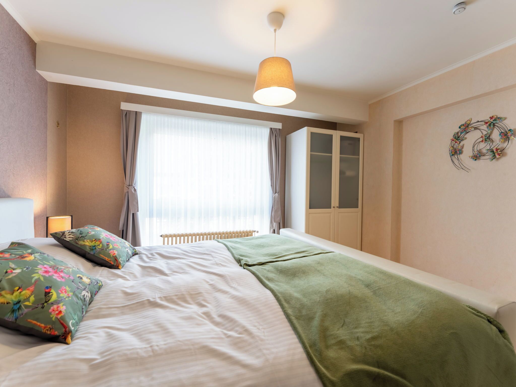 Une chambre à coucher avec un lit, un radiateur, une armoire et une fenêtre avec des rideaux.