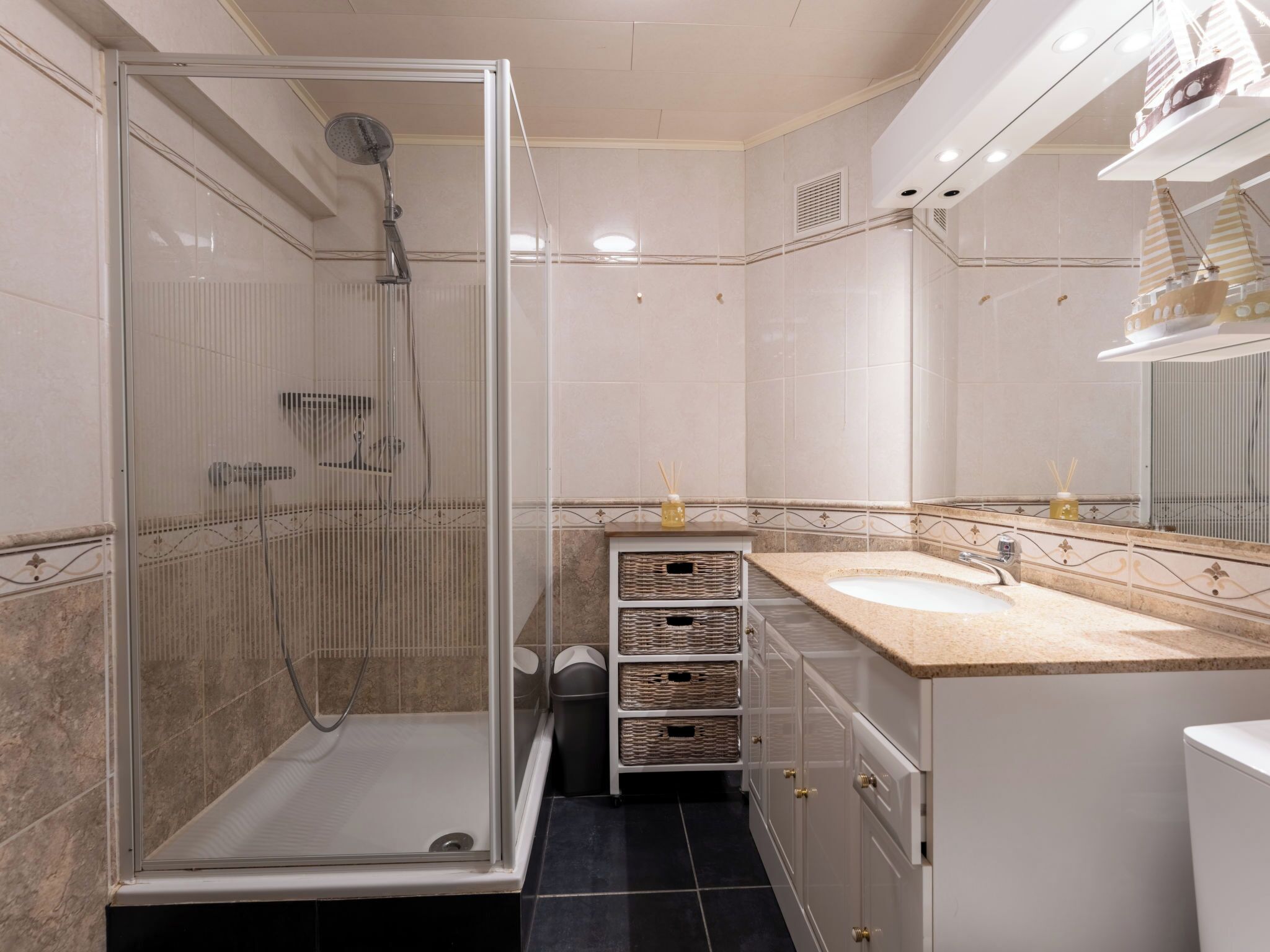 Un baño con ducha de vidrio, lavamanos con espejo y armarios de almacenamiento.
