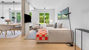 Een moderne woonkamer met een bank, een salontafel en een televisie. Er is een eethoek met een tafel en stoelen.
