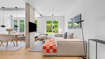 Een moderne woonkamer met een bank, een salontafel en een televisie. Er is een eethoek met een tafel en stoelen.