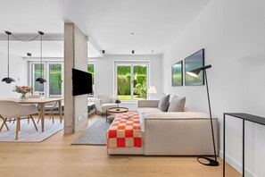 Ein modernes Wohnzimmer mit Sofa, Couchtisch und Fernseher. Ein Essbereich mit Tisch und Stühlen ist ebenfalls vorhanden.
