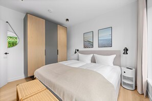 A modern bedroom with a large bed, a wardrobe, a bedside table, and two wall-mounted pictures. - Arriving between the sea, the light, and the open landscape (List auf Sylt)