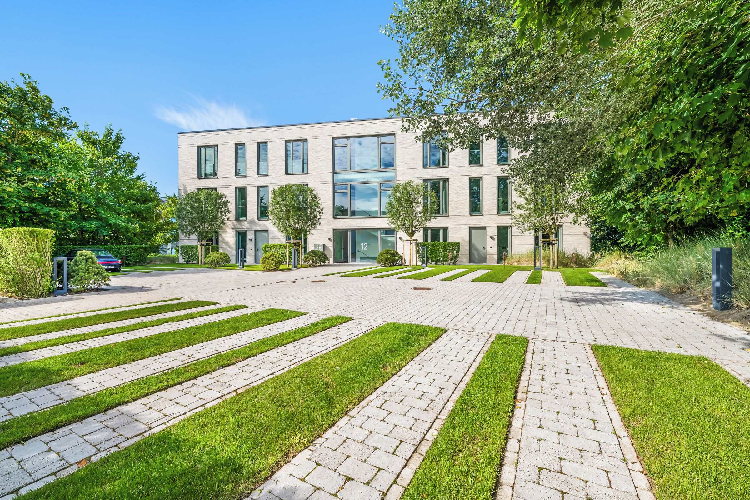 Un edificio moderno con un cortile lastricato, prati verdi e un cielo azzurro limpido.
