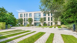 Een modern gebouw met een verharde binnenplaats, groene gazons en een heldere blauwe lucht.